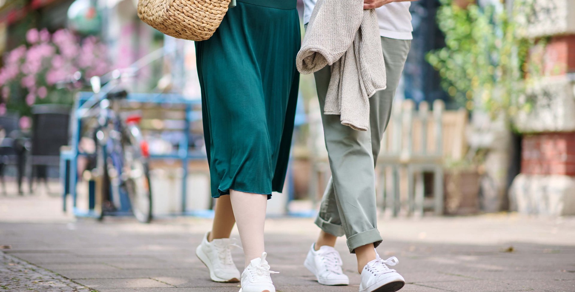 Ein Paar geht entspannt durch eine sommerliche Stadt. Beide tragen weiße Sneakers, und die Frau trägt wirksame Kompressionsstrümpfe aus der VenoTrain Special-Linie.