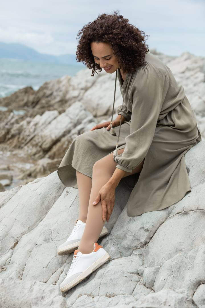 Auf dem Bild ist eine Frau zu sehen, die auf einem Fels sitzt und sich an die Wade fasst. Sie trägt VenuTrain soft Kompressionsstrümpfe von Bauerfeind.