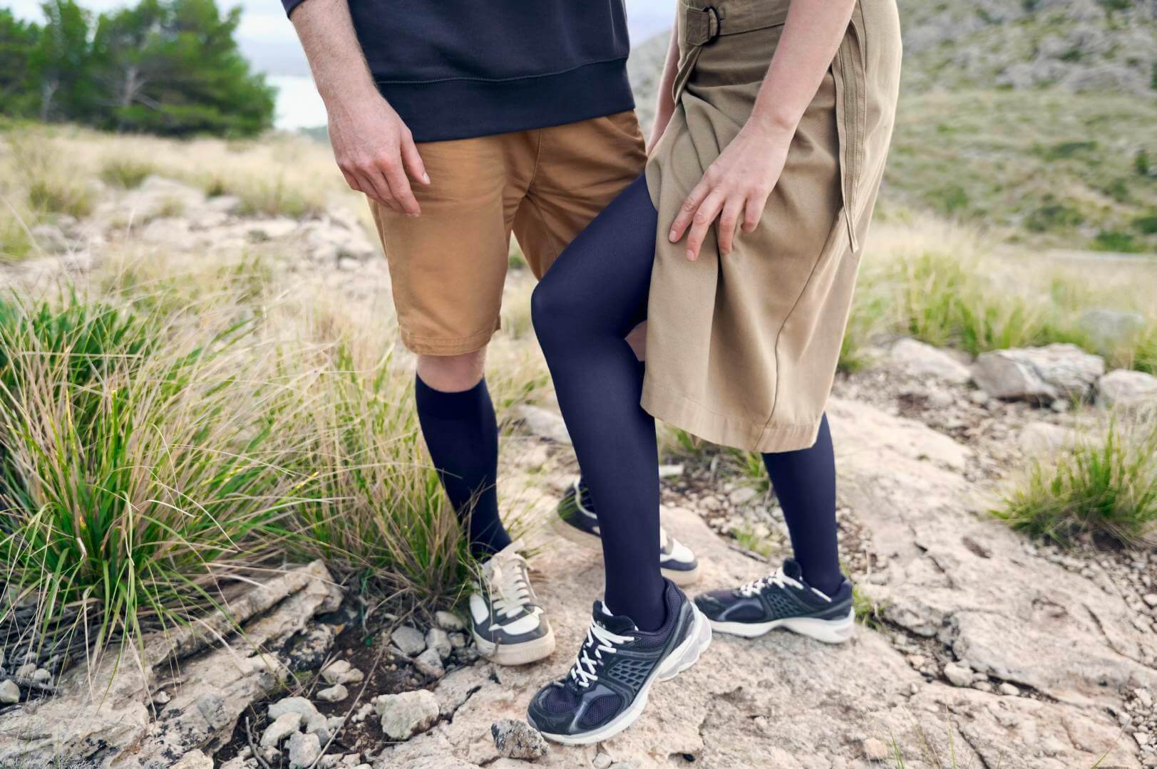 Nahaufnahme eines Paares, das auf einem felsigen Wanderweg steht. Beide tragen sportliche Outfits in Erdtönen mit passenden VenoTrain Kompressionsstrümpfen in Dunkelblau.