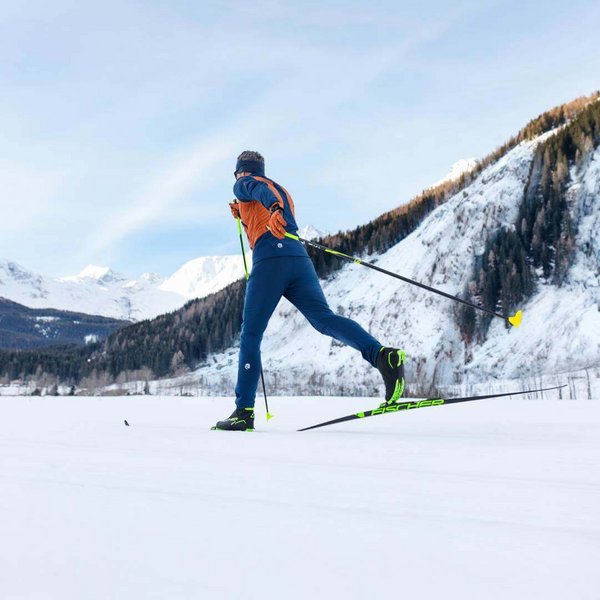 Je herkent een man tijdens het langlaufen. Hij skiet in een besneeuwd berglandschap. Langlaufen is een gewrichtsvriendelijke sport voor de winter.