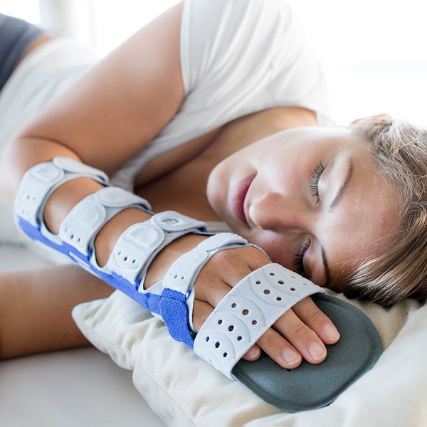 Een vrouw ligt op haar zij op een wit kussen en slaapt. Ze draagt een ManuLoc long Plus aan haar rechterarm en hand, die met klittenband bevestigd is.