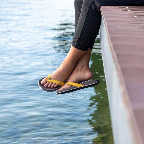 Uitsnede van twee benen die vanaf een houten steiger boven het water van een meer bungelen. Aan de voeten draagt de persoon een paar ErgoPad:ID teenspreiders van Bauerfeind.