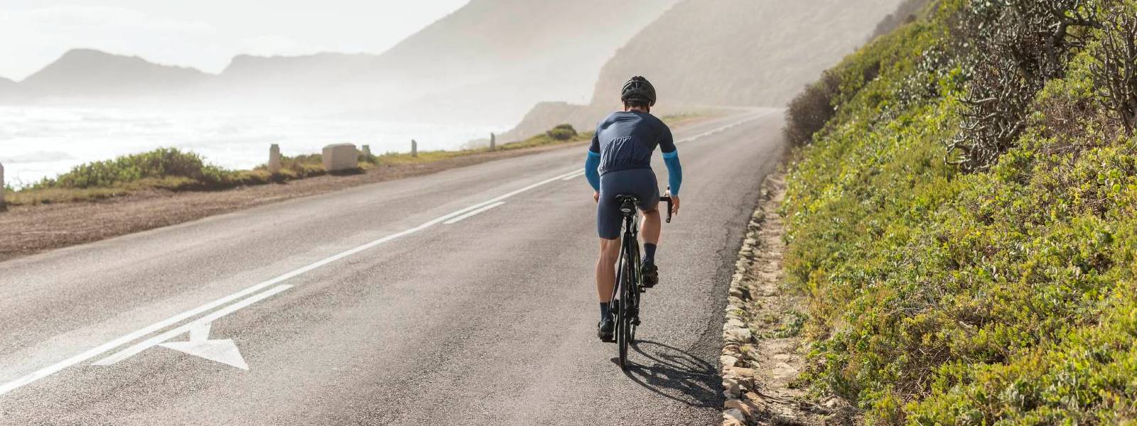 Fietsers dragen blauwe armmouwen en rijdt op een straat op de helling met een uitzicht op zee