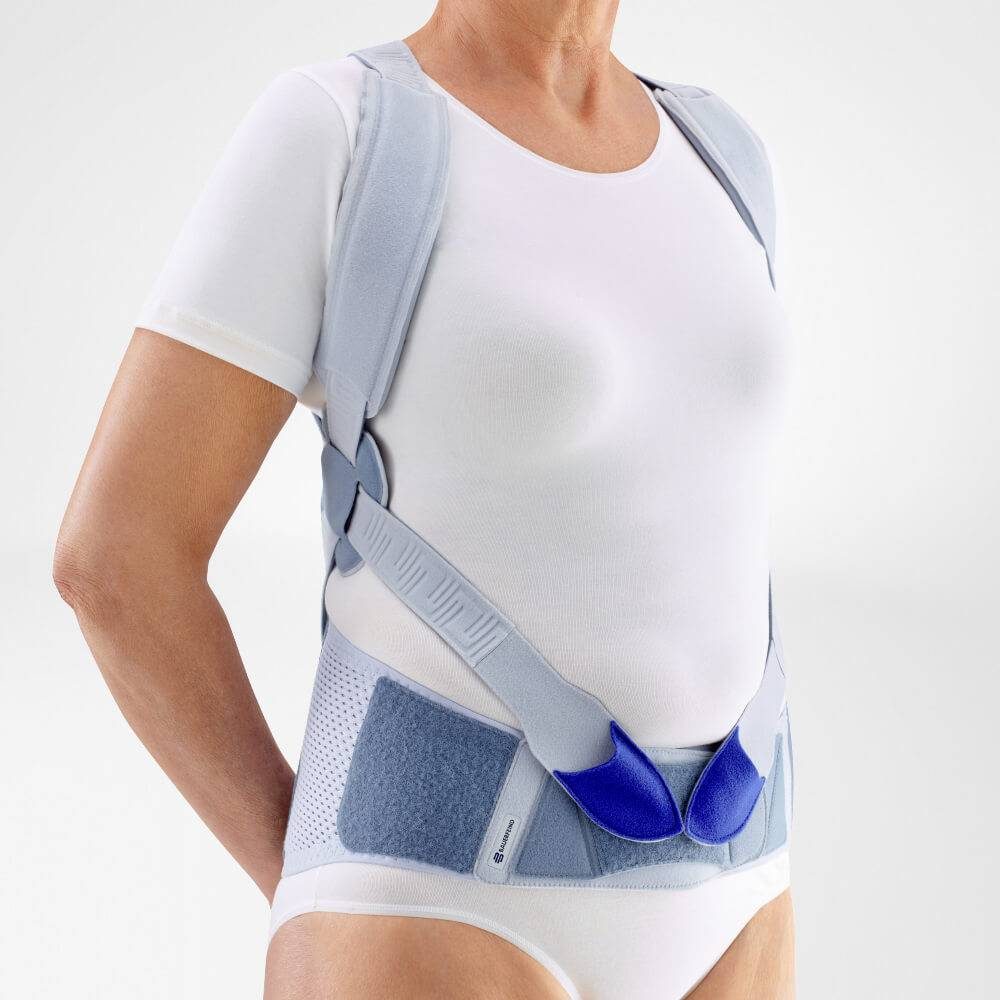 Bovenlichaam met een lichtblauwe steunbrace rond schouders, rug en buik over witte kleding.