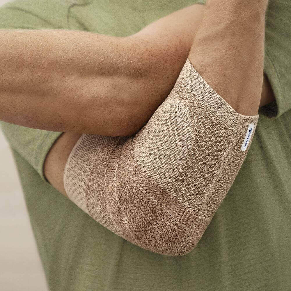 Uitsnede van een persoon met een groen T-shirt die vanwege een tenniselleboog rekoefeningen uitvoert. De persoon draagt een EpiTrain, een pijnverlichtende elleboogbandage van Bauerfeind, in de kleur beige.