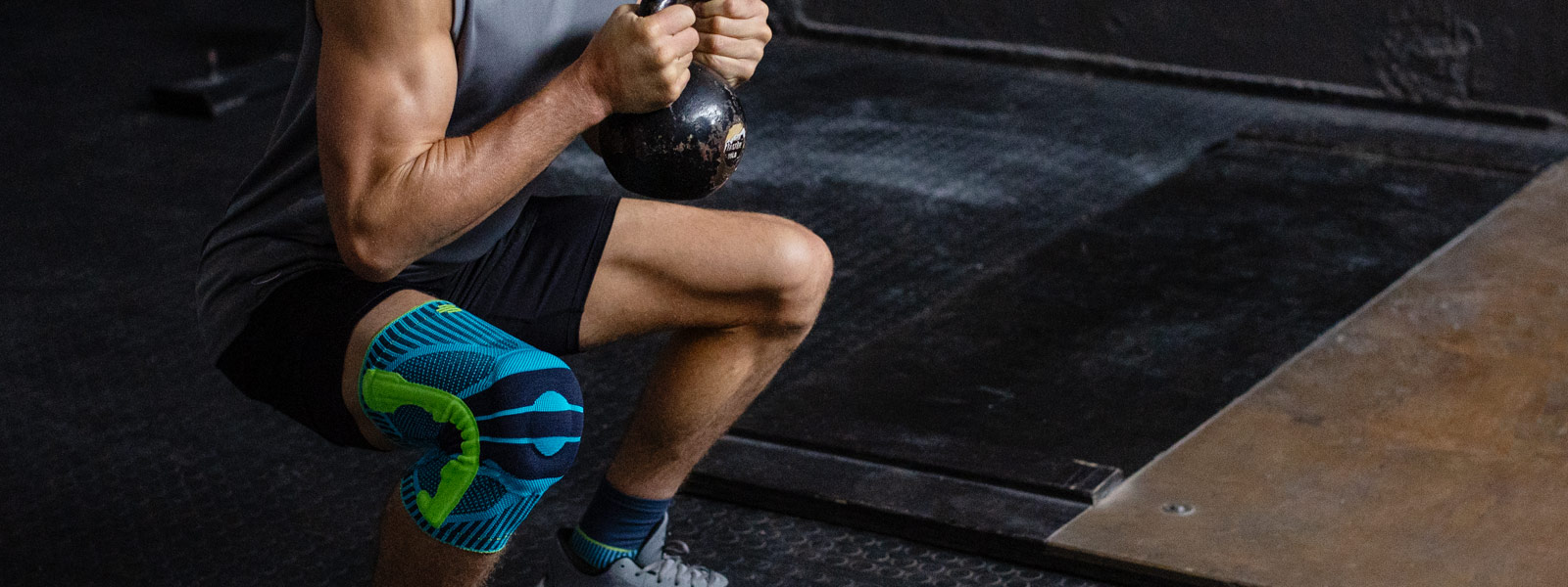 Man met een kneebord gaat diep gehurkt met een kettlebell tussen de twee handen