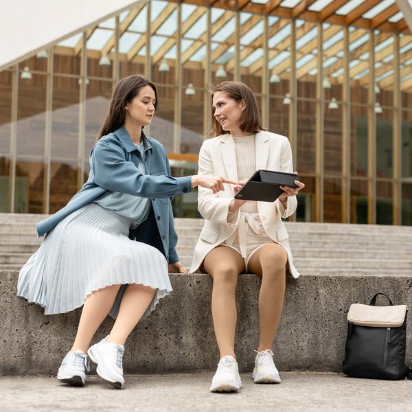 Op de afbeelding zitten twee vrouwen op een stenen muurtje. Ze praten met elkaar. Beiden dragen VenoTrain micro compressiekousen van Bauerfeind.