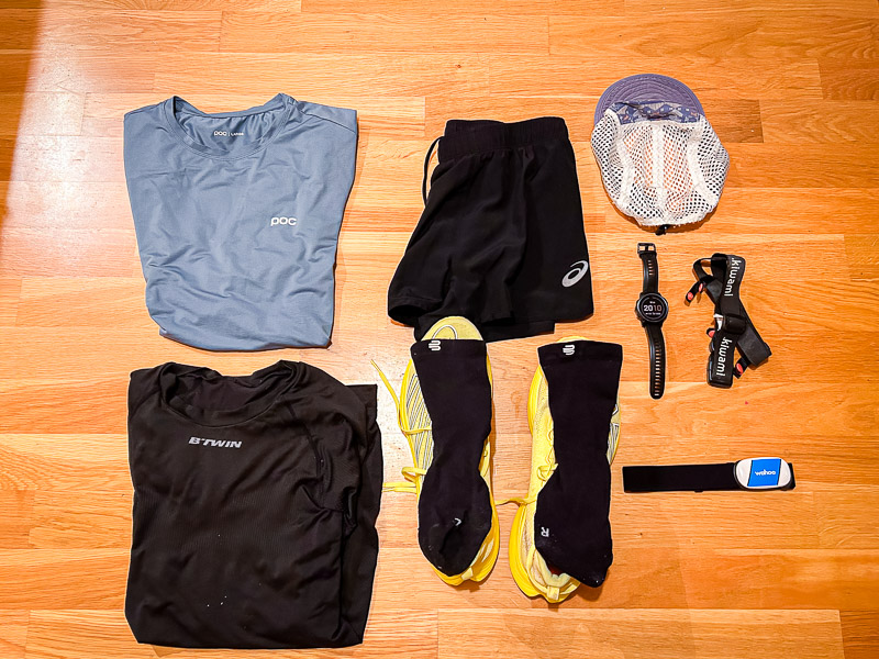 Voorbereidingen voor de halve marathon: Een volledige race-outfit, inclusief blauwe hardloopkleding, gele hardloopschoenen en technische accessoires zoals een hartslagmonitor en een hardloophorloge, ligt klaar.