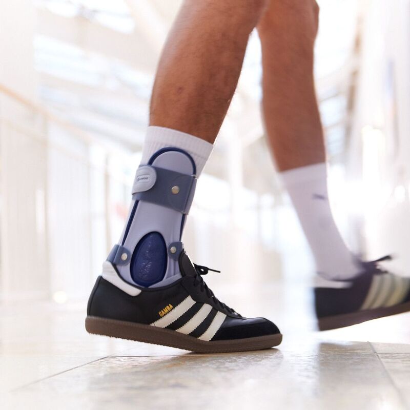 Persoon loopt met orthopedische enkelbrace en zwarte sneakers, geschikt voor in schoenen.