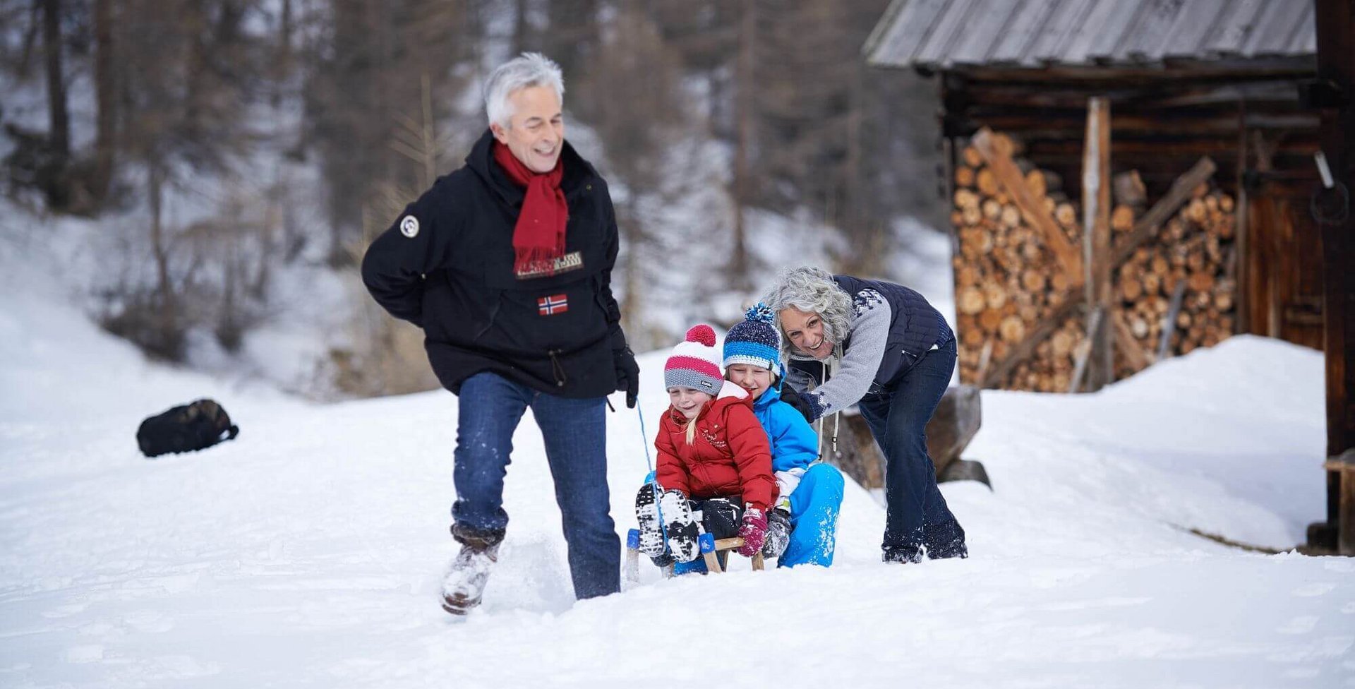 Een ouder echtpaar trekt twee kinderen, die op een slee zitten, door de sneeuw. Al eenvoudige bewegingen zoals bukken, draaien of overeind komen kunnen het lendenwervelkolom-syndroom (kortweg: LWK-syndroom) uitlokken.