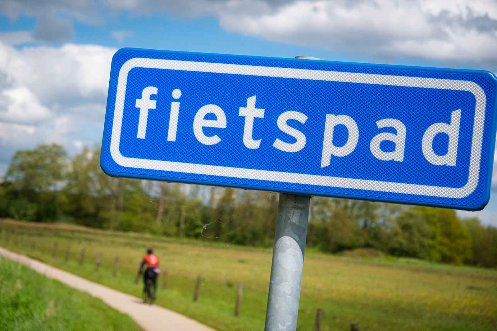 Op de voorgrond staat een bord met het opschrift "Fahrradweg" (fietspad) en, onscherp, een fietser op het fietspad eronder