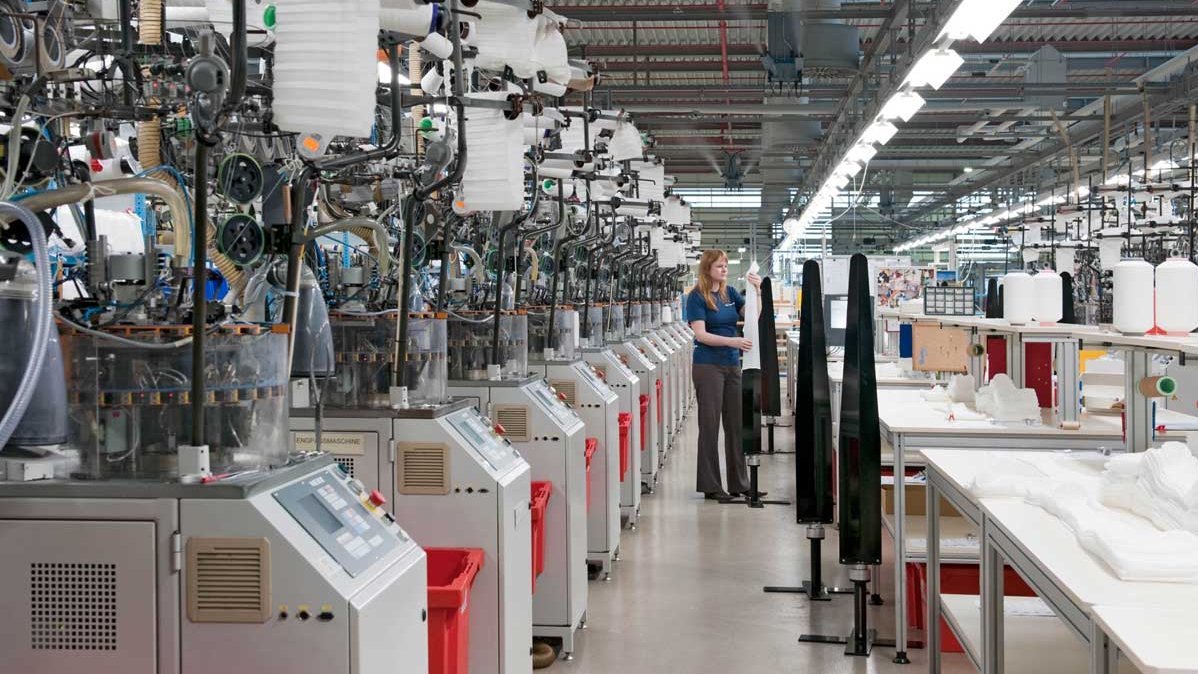 Binnenaanzicht van de productiehal bij Bauerfeind: medewerkers bedienen machines en installaties, meerdere werktafels zijn voorzien van gereedschap en materialen.