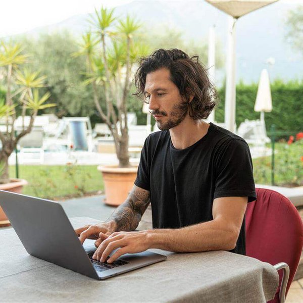 Op de afbeelding zie je een jonge man die aan een laptop werkt. Monotone bewegingen op het werk kunnen klachten van een muisarm veroorzaken.