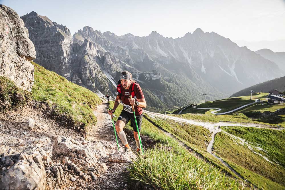 Ultraloper tijdens een steile klim met loopstokken op een alpiene bergtrail