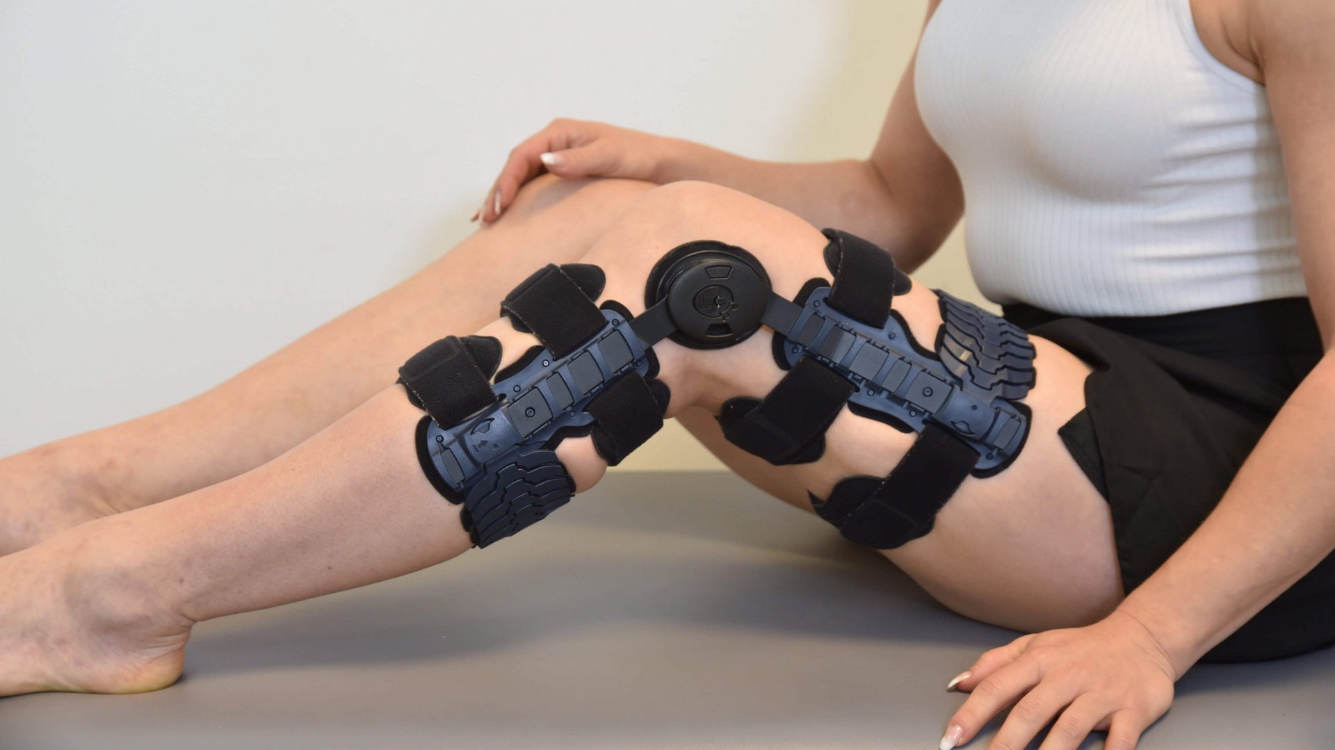 Anne-Maria Kot zit op de grond, haar linkerbeen is naar voren gestrekt en voorzien van een zwarte SecuTec Genu Flex knie-orthese.