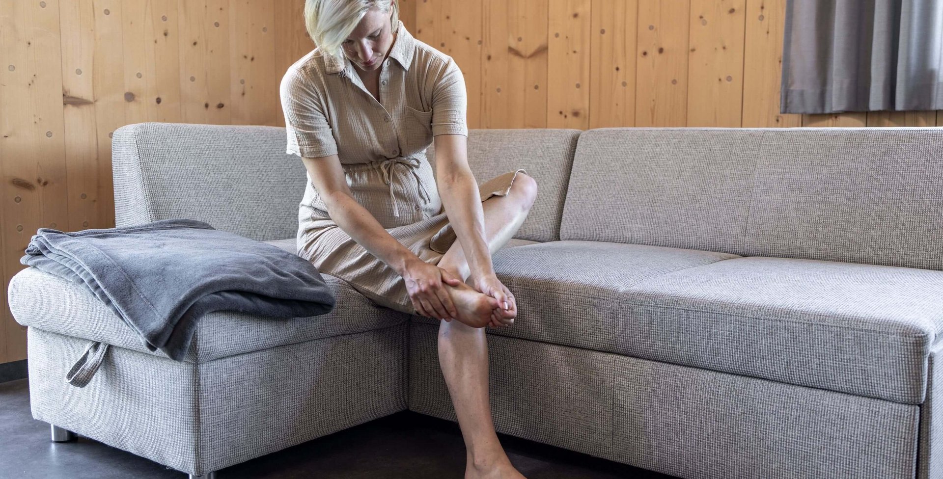 Een zwangere vrouw zit op een bank en masseert haar pijnlijke voet om klachten te verlichten.