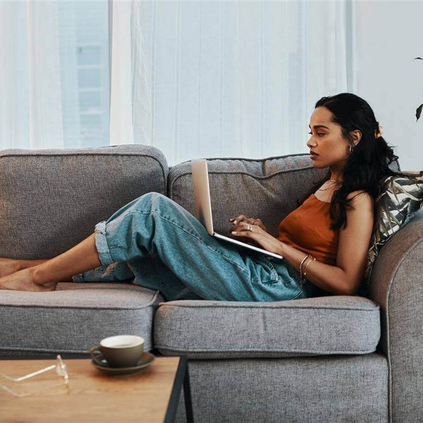 Op de afbeelding zie je een vrouw die met een laptop op de bank ligt. Ontdek welke gezondheidsgevolgen te weinig beweging kan hebben.