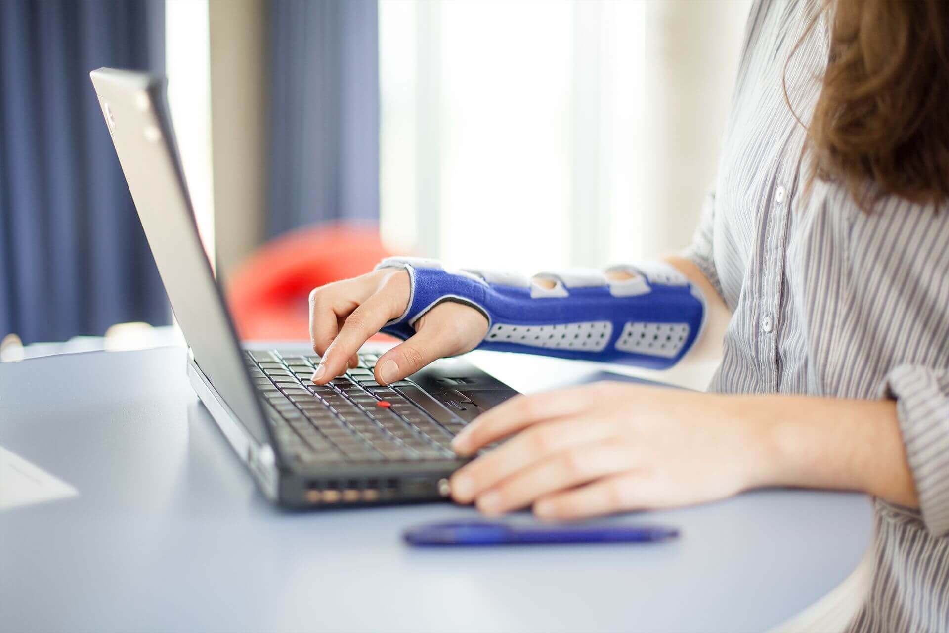 Beelduitsnede van een vrouw die aan haar laptop werkt. Ze draagt een ManuLoc long, een stabiliserende polsorthese van Bauerfeind, aan haar rechterarm. Die biedt onder andere na een radiusfractuur ondersteuning.
