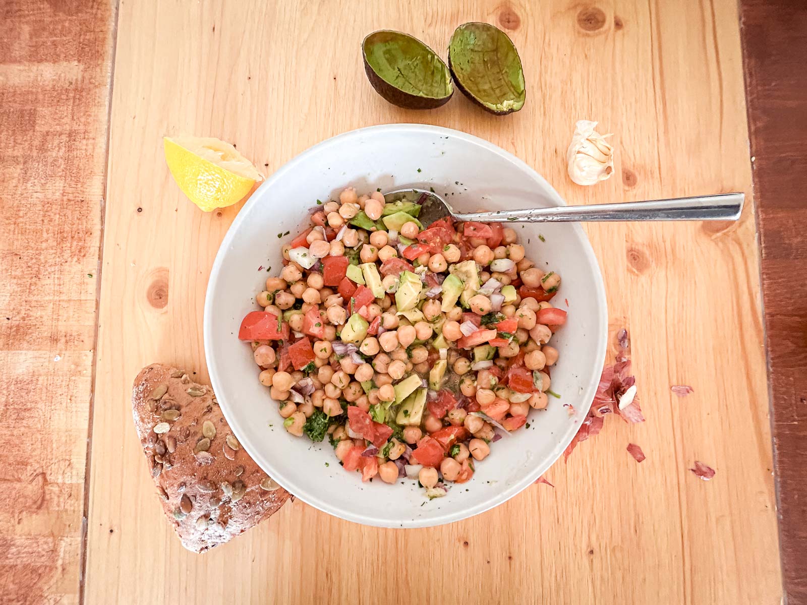 Een kom kikkererwtensalade omgeven door verse ingrediënten zoals avocado, citroen en brood. Ideaal voor een gezonde en voedzame maaltijd na de training.