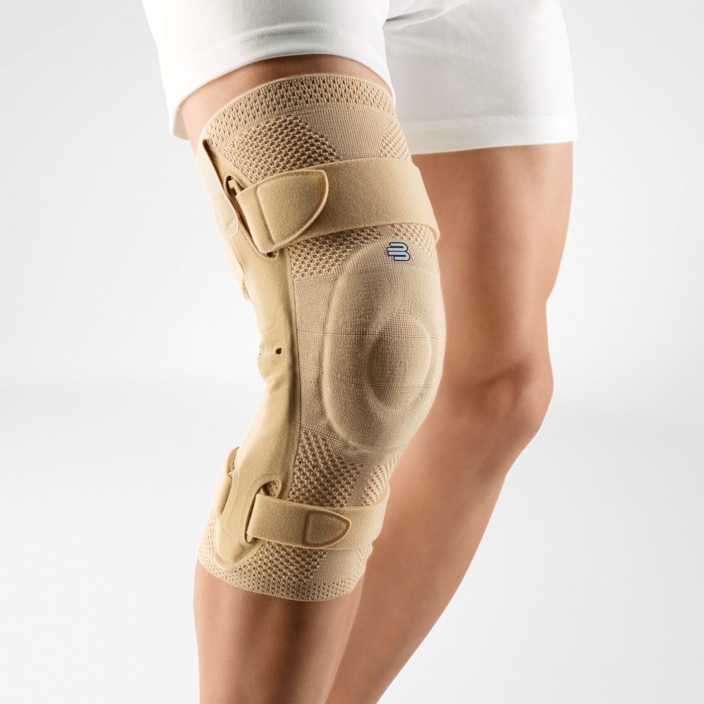 Beige kniebrace met klittenbandbanden om een gebogen knie, gedragen onder een witte korte broek.