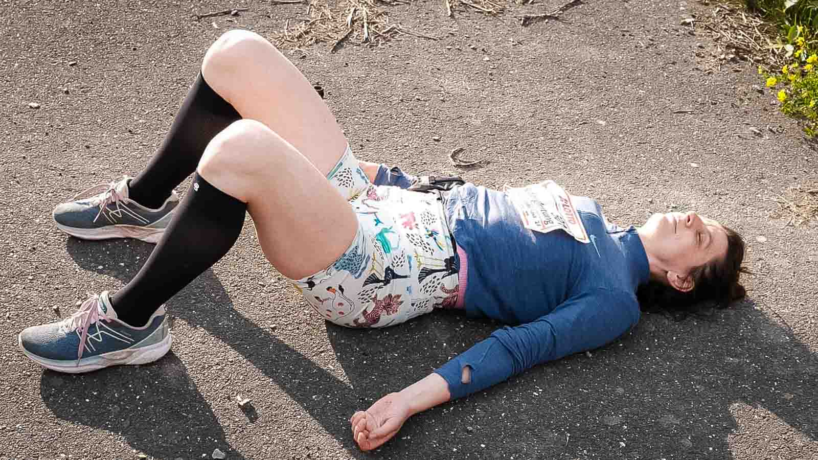 Een vrouw in kniekousen ligt uitgeput op de grond met haar benen gebogen na de Rennsteigloop