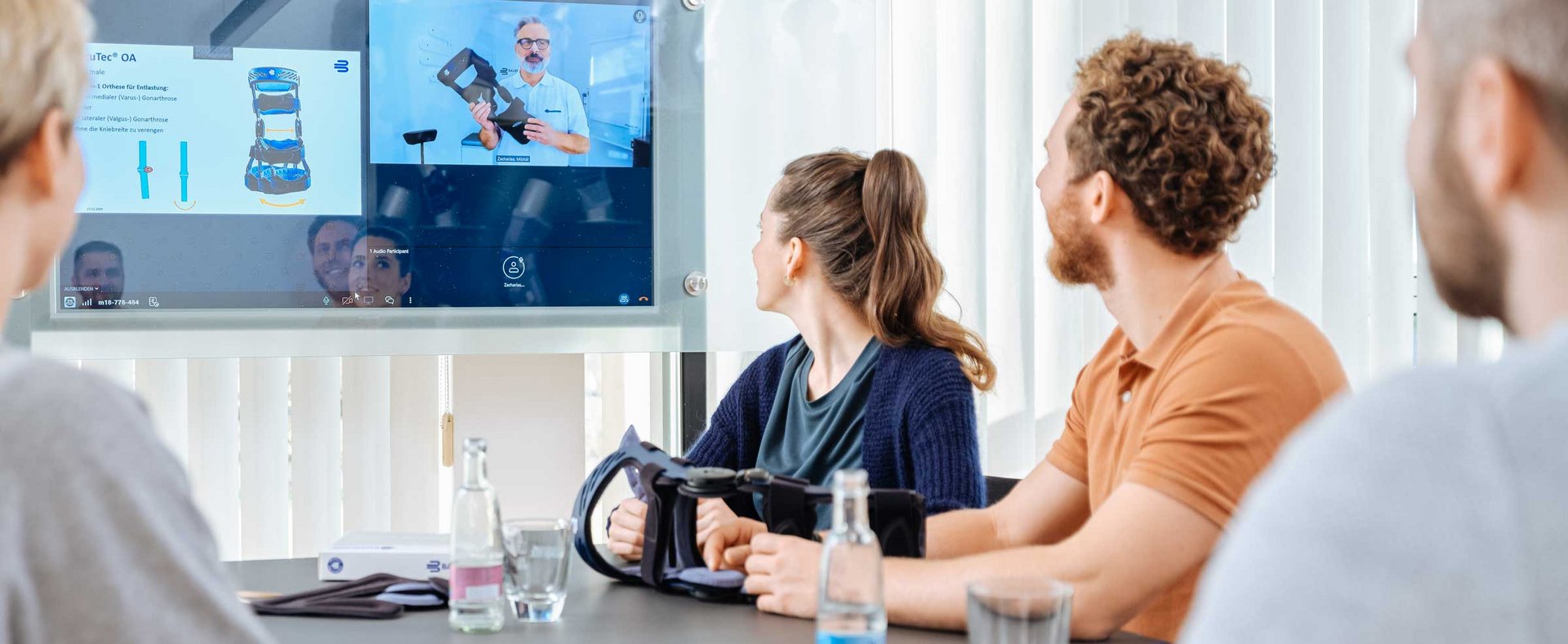 Meerdere personen zitten in een trainings- of webinarruimte en kijken naar een groot projectiescherm waarop content wordt gepresenteerd. Op de voorgrond zie je hoofden van de deelnemers aan de training.
