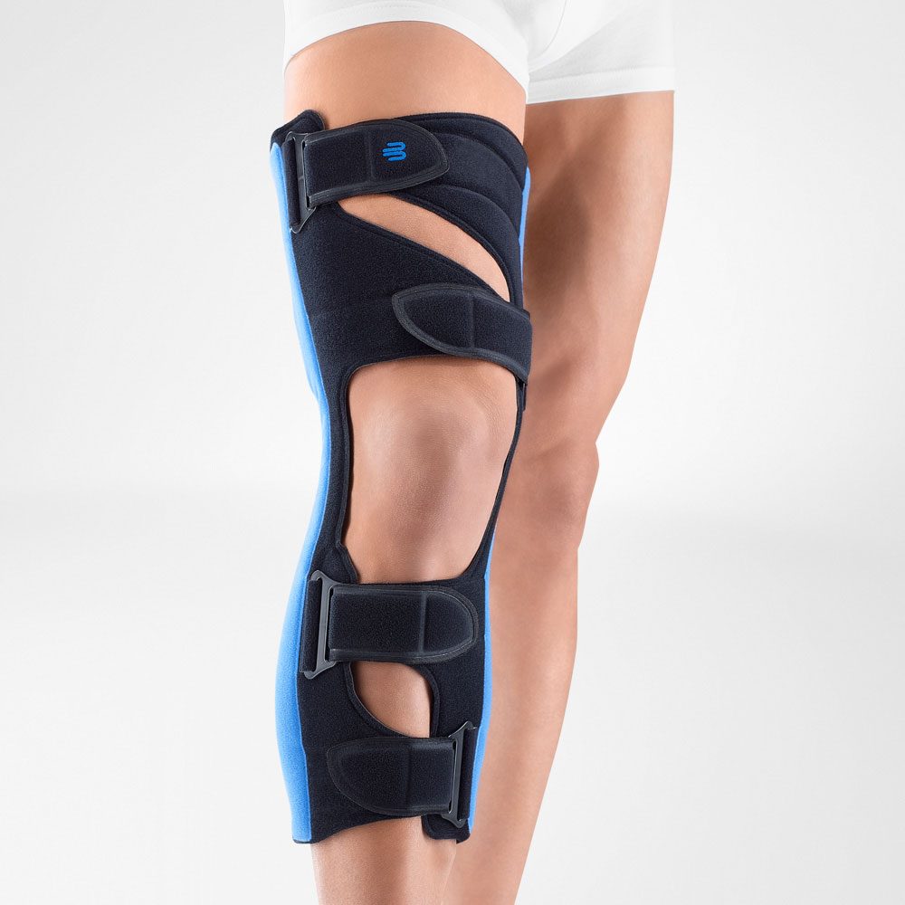 Been met zwarte en blauwe kniebrace met meerdere klittenbandriemen, gedragen onder een witte korte broek.