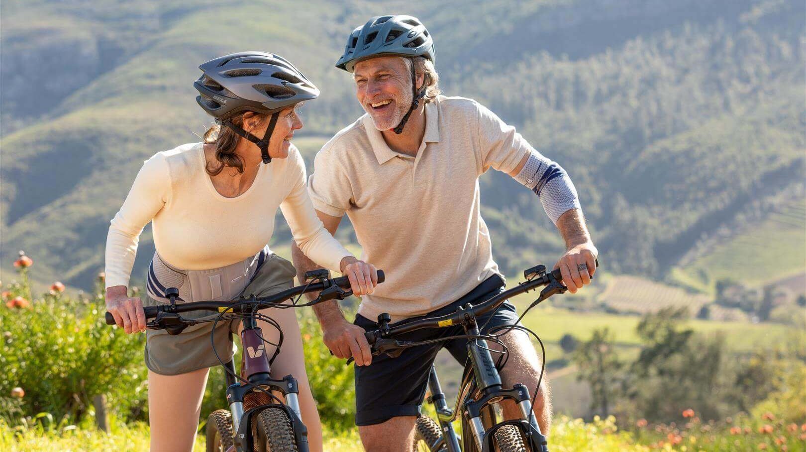 Afgebeeld is een ouder stel dat een fietstocht maakt. Om lage rugpijn te voorkomen draagt de vrouw een LumboTrain rugbandage van Bauerfeind.