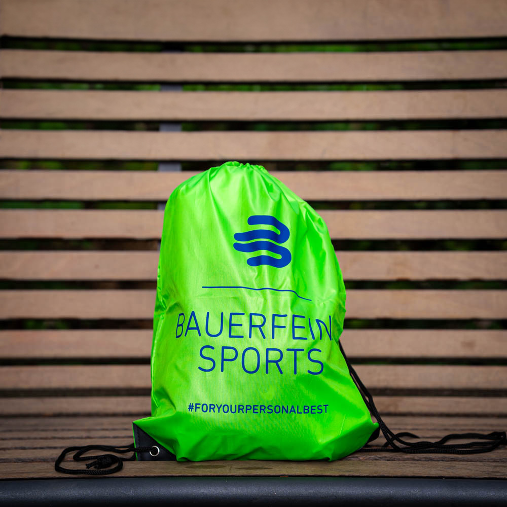 Een groene Bauerfeind Sports gymtas ligt op een houten bank, met het logo en de hashtag #foryourpersonalbest zichtbaar.
