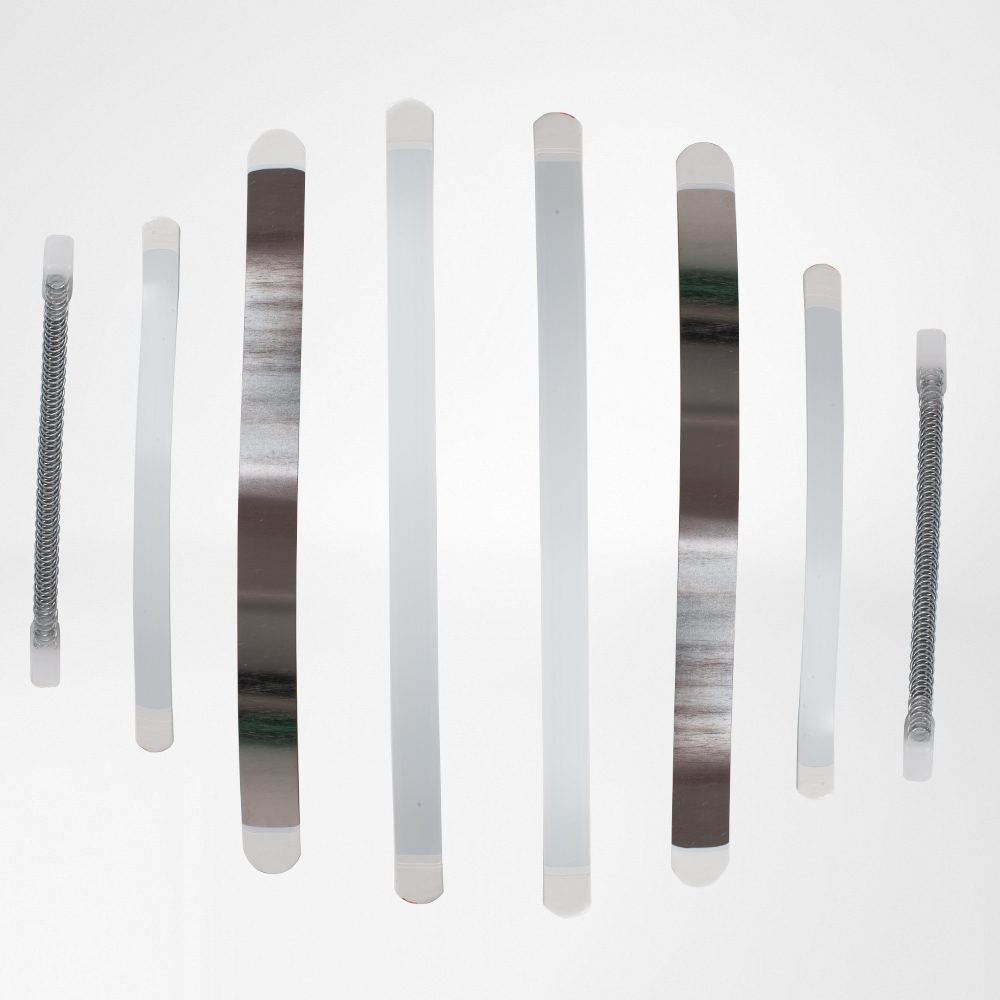 Acht langwerpige kunststof- en metalen strips, waaronder twee met spiraalveren, op een witte achtergrond.