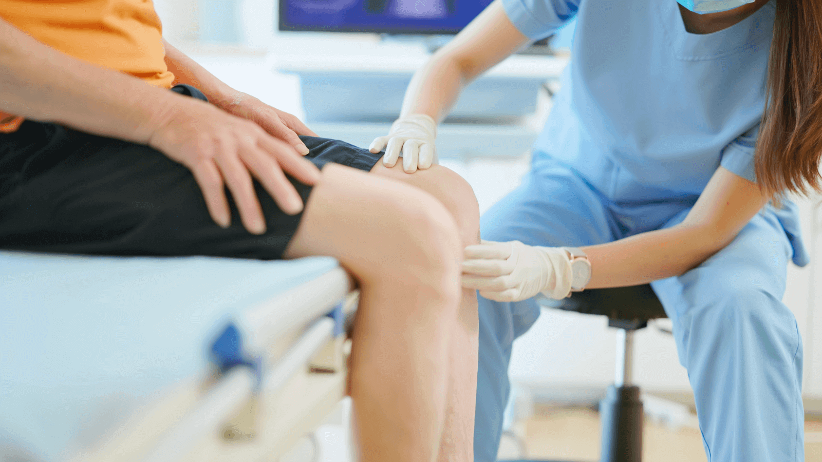 Het beeld toont een arts die de knie van een patiënt onderzoekt.