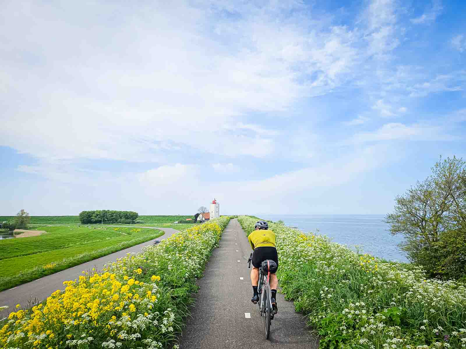 Een fietser rijdt over een prachtig fietspad langs de zee, in de richting van een vuurtoren