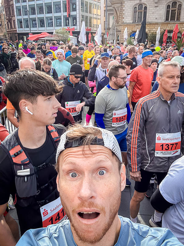 Een opgewonden deelnemer maakt een selfie vlak voor de start van de Mitteldeutscher Marathon 2024 in Halle. Om hem heen verzamelen veel andere hardlopers zich, klaar voor de halve marathon.