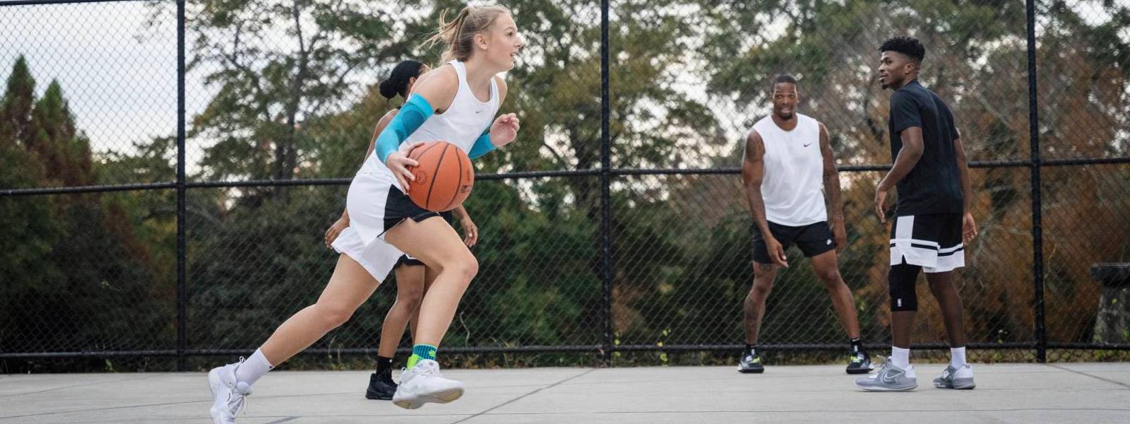 Basketbalspeler dribbelt langs haar tegenstanders op een vrije ruimte en draagt ​​blauwe arm mouwen