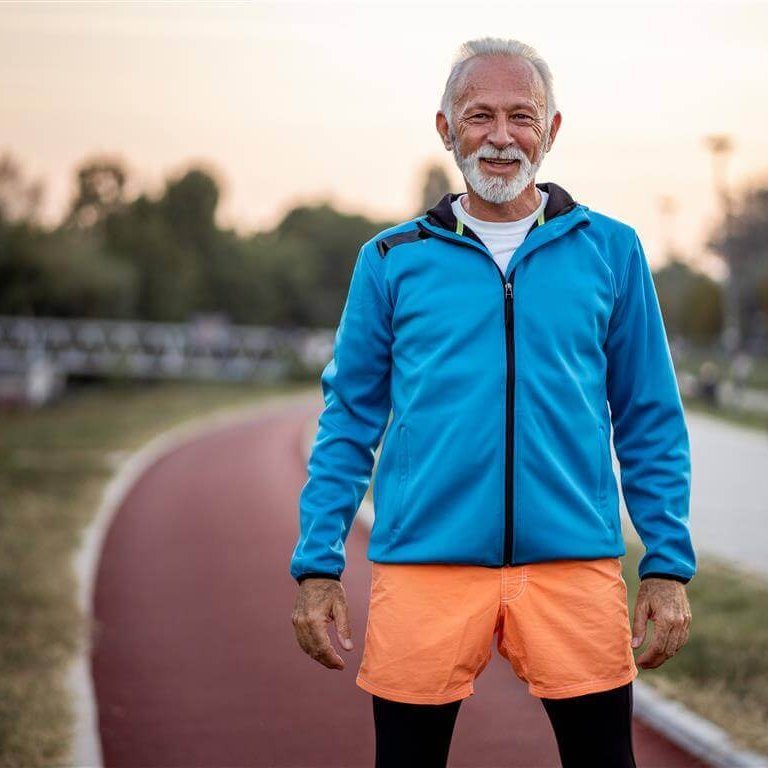 De foto toont een oudere man in een sportoutfit op een sportveld. Hij blijft in beweging om de pijn door artrose onder controle te houden.