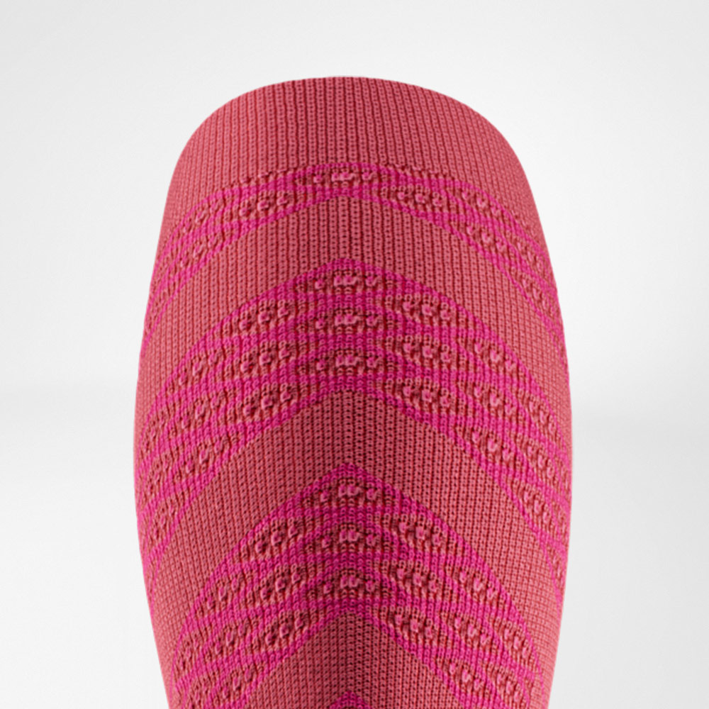 Close-up van een roze compressiesleeve met fijn breisel en patroon, speciaal ontworpen om de kuitspieren tijdens het lopen te ondersteunen.
