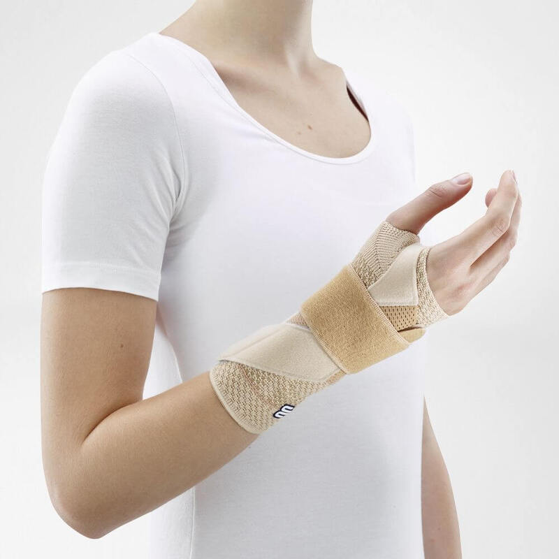 Vrouw draagt beige Bauerfeind ManuTrain polsbrace voor discrete polsondersteuning.
