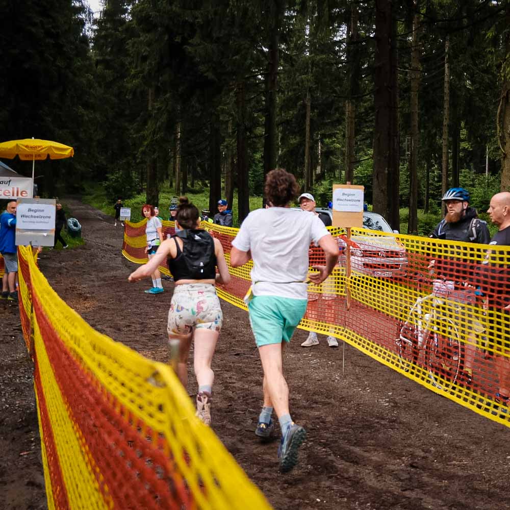 Een man en een vrouw lopen door het bos, gadegeslagen door voorbijgangers, terwijl de grond modderig is