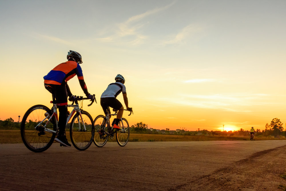 Twee race fietsers rijden de zonsondergang in op een vlakke betonnen weg