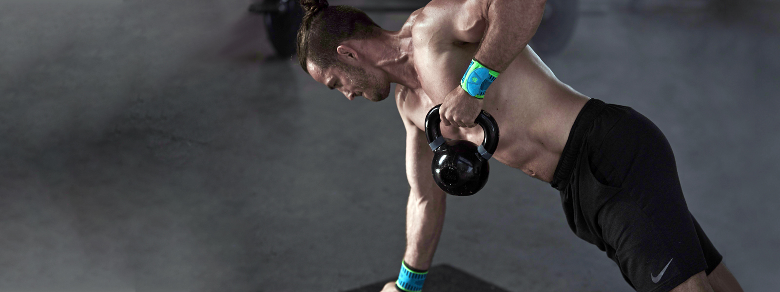 Atletische man met gratis torso- en polsbandjes treinen met de kettlebell en de ene hand ondersteunt de andere trekt de kettlebell