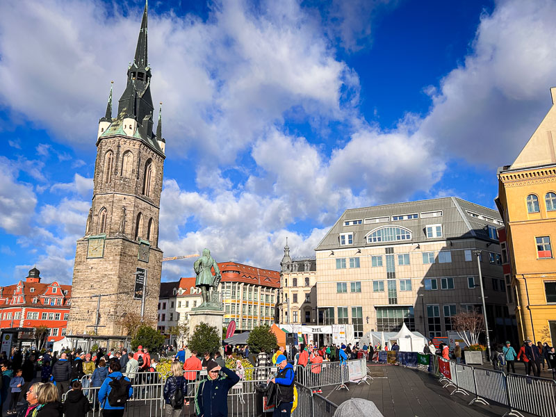 Lopers en toeschouwers verzamelen zich op het marktplein van Halle voor de start van de Centraal-Duitse Marathon. Op de achtergrond staat de iconische Rode Toren, een herkenningspunt van de stad.