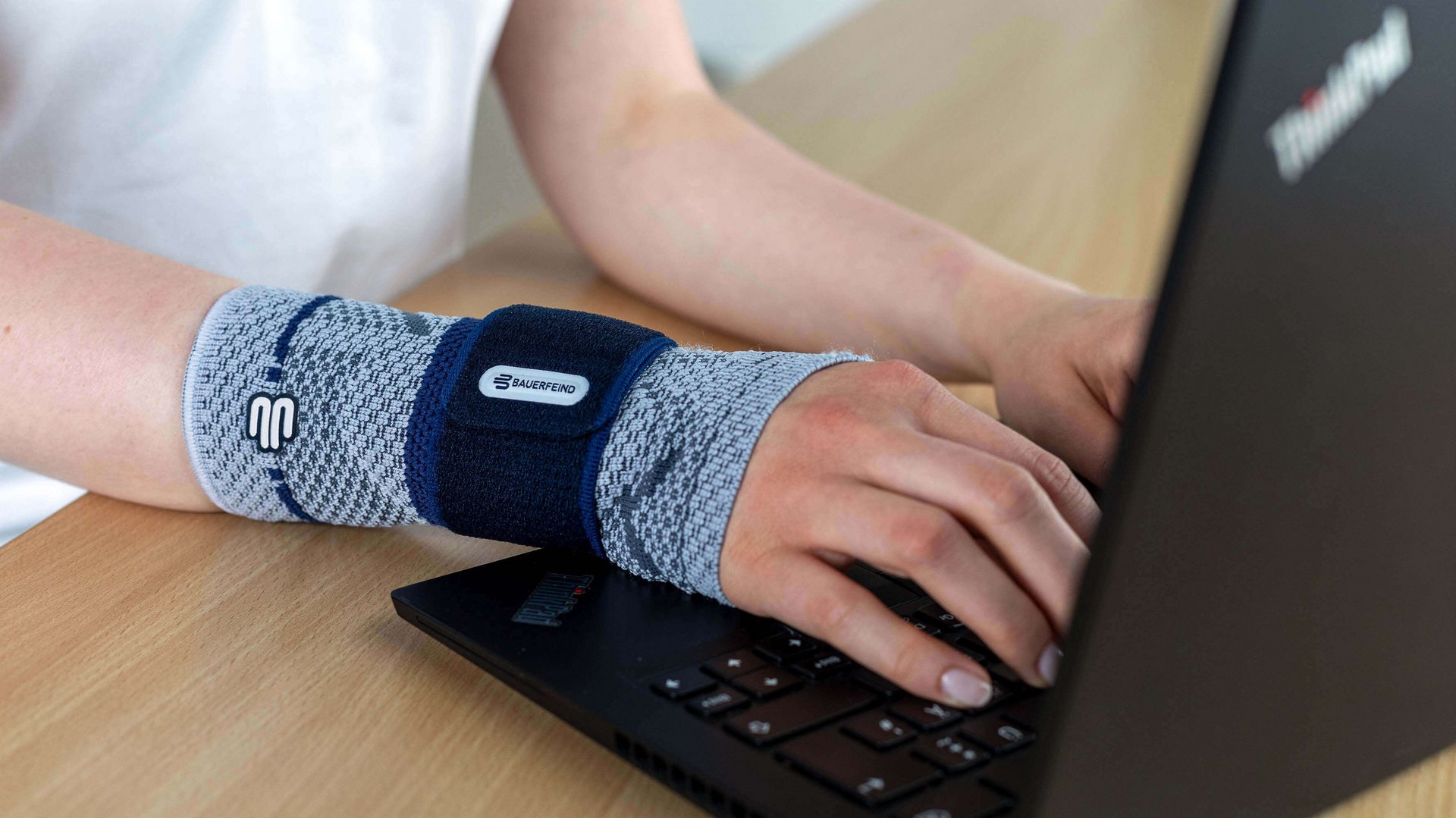 Detailopname van een vrouw aan de laptop, die om haar rechterpols een ManuTrain bandage van Bauerfeind draagt. Die biedt ondersteuning bij muisarmklachten.