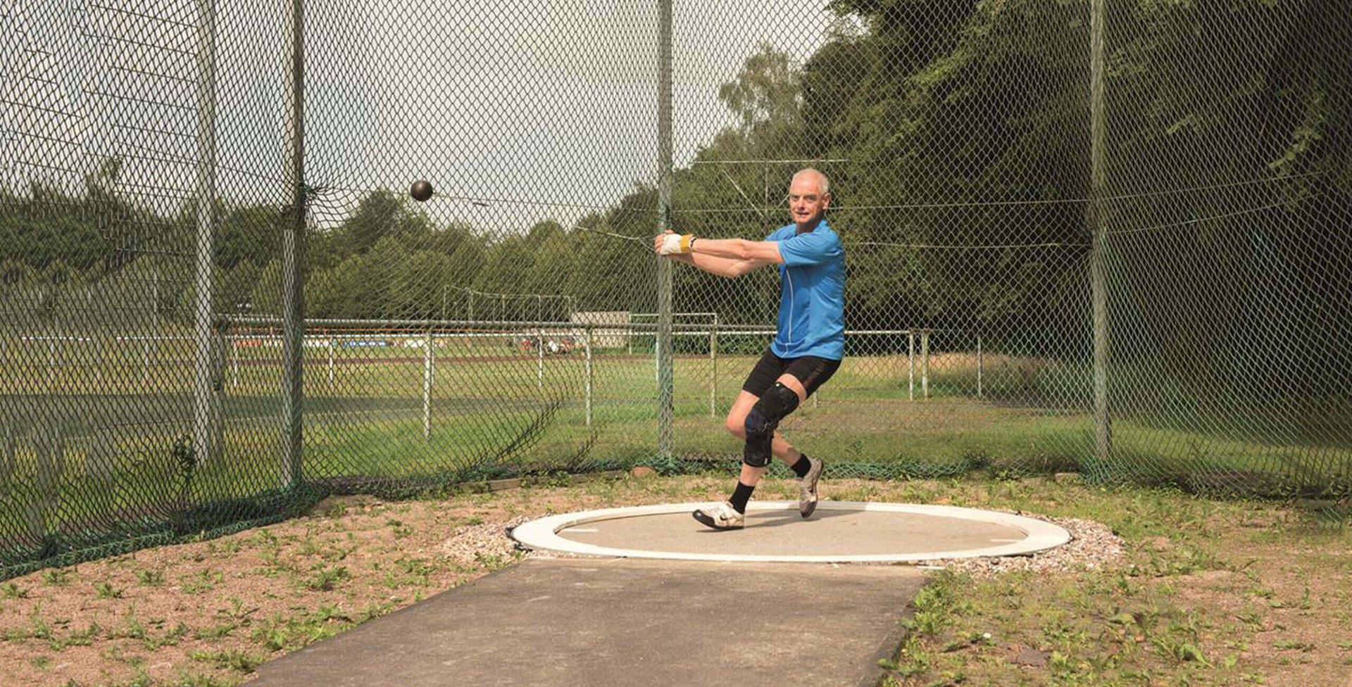 De afbeelding toont sporter en artrosepatiënt Wilhelm Kraatz met de knieorthese GenuTrain OA tijdens het kogelslingeren.