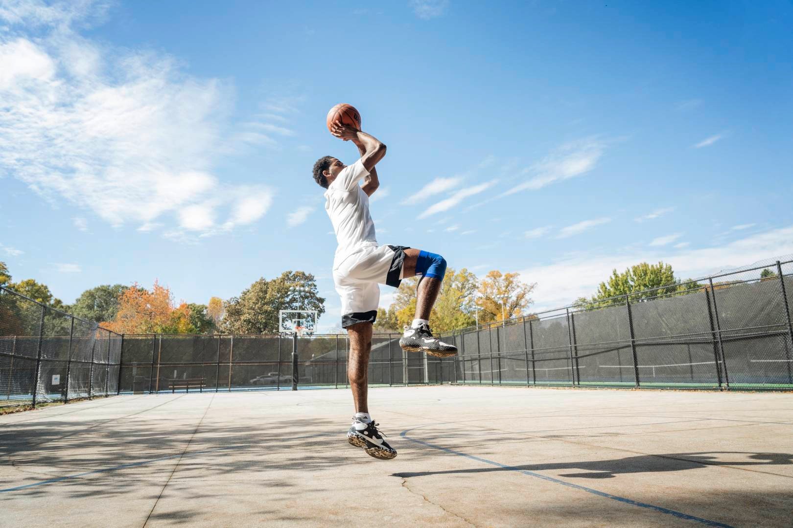 Basketbalspelers springen op een straatveld voor de worp uit handen met de bal over het hoofd, gebogen in de andere, laten de andere verticaal naar beneden zien