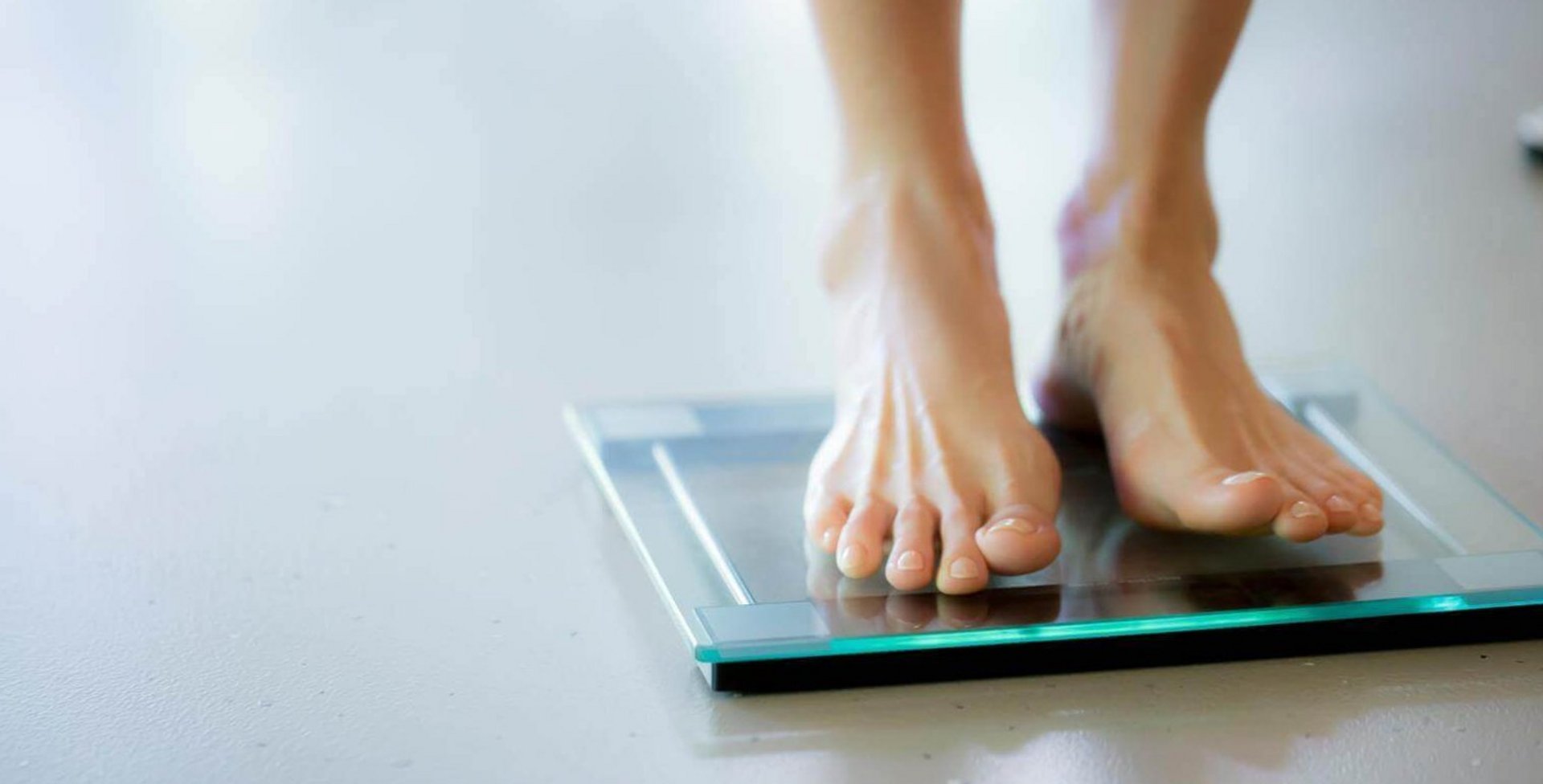 Vrouwenvoeten staan op een digitale glazen weegschaal op een lichte vloer.