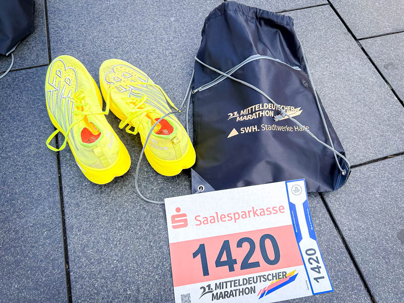 Racedag bij de halve marathon: Gele hardloopschoenen naast het startnummer en een sporttas van de 21e Mitteldeutscher Marathon, klaar om te gaan.