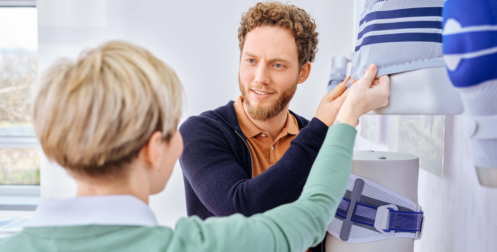 Een adviseur laat een geïnteresseerde patiënte de rugbandages van Bauerfeind zien in een showroom.