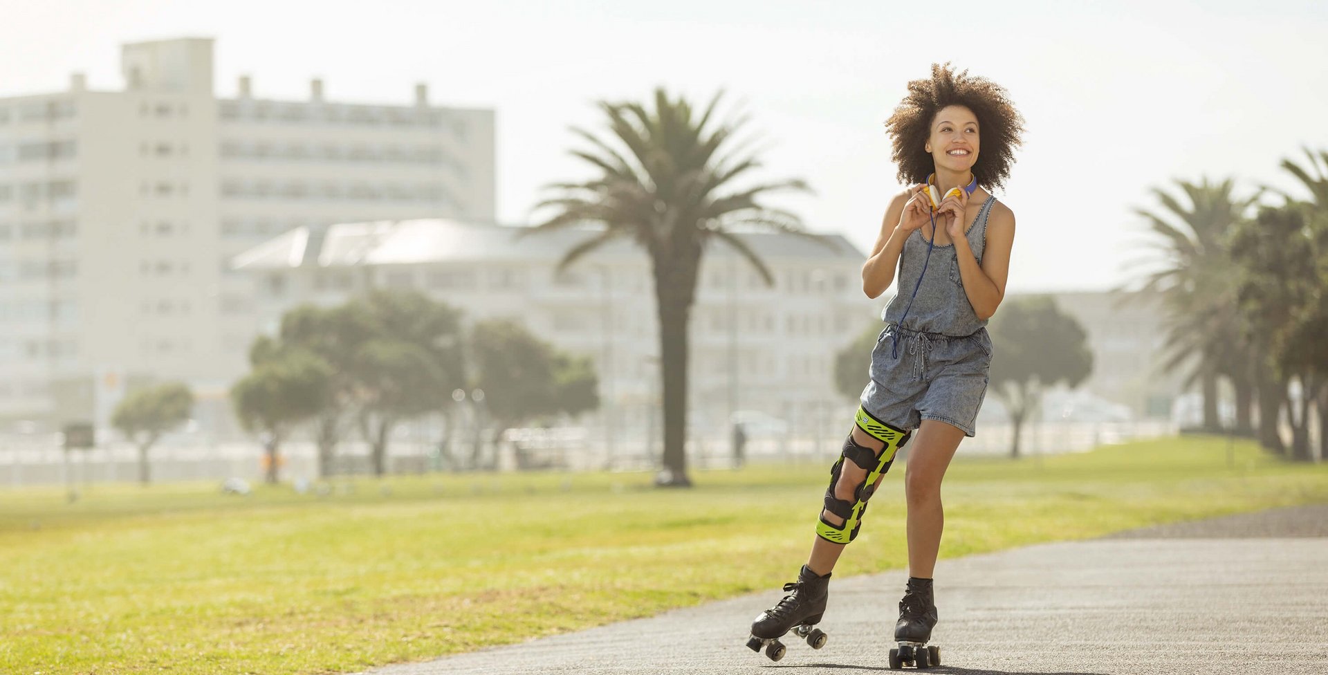 De afbeelding toont een lachende, jonge vrouw op rolschaatsen op een strandboulevard. Op haar knie draagt ze een SecuTec Genu. Deze orthese biedt onder andere ondersteuning na een Unhappy Triad.