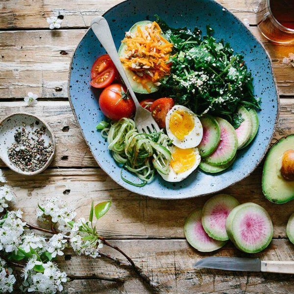 De afbeelding toont een houten tafel met een bord waarop verschillende gezonde levensmiddelen zijn aangericht. Een uitgebalanceerde voeding is een belangrijk onderdeel van de lip- en lymfoedeembehandeling.