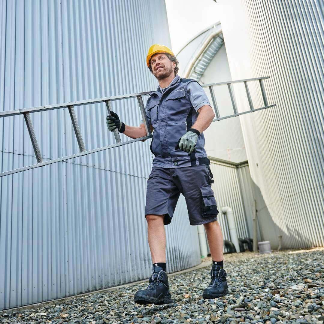 Een bouwvakker draagt een ladder tussen silo's.
